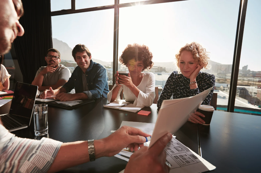 Group of 5 individual sitting at a large table having business negotiations