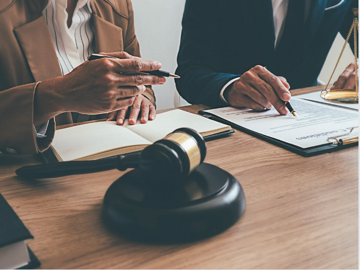 hands of 2 people sitting at a table with court gavel and legal documents