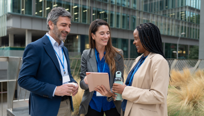 Three people, a man and 2 women, standing having business conversation outside, smiling pleasantly