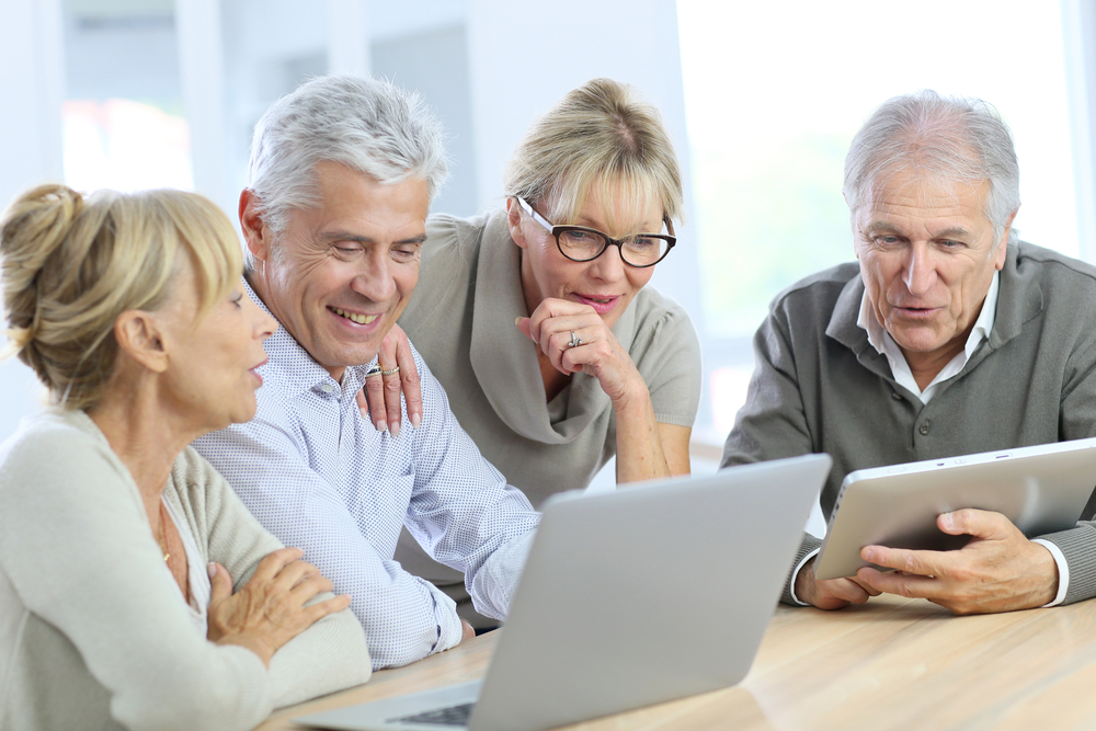 Two grey-haired men and women look at a laptop. They are discussing the benefits of language training at an older age.