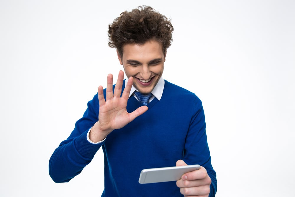 Male language instructor wearing a sweater and tie saying hello to students on his mobile device during a language lesson