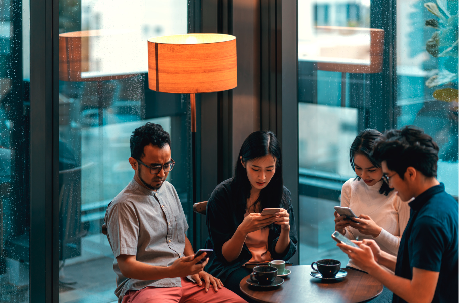 Group of 4 disengaged coworkers sitting around a table focused only on their smartphones