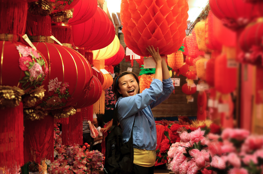 Smiling girl standing amid various chinese new year decorations like red paper lanterns and flower arrangements 
