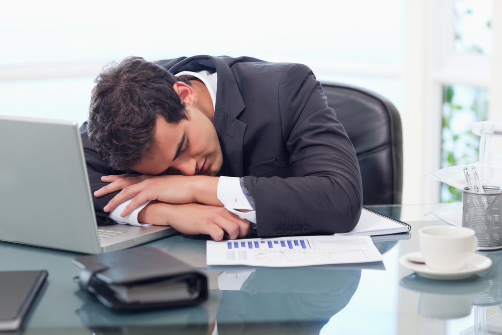 Man in business suit laying head on desk due to lack of employee engagement