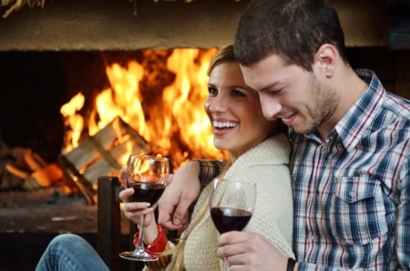 Man and woman having red wine in front of a fireplace during virtual language experiences