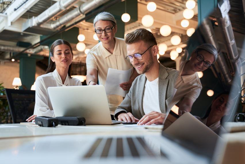 Two women and one man on a leadership team sit at a work table with a laptop and review their workforce development strategy